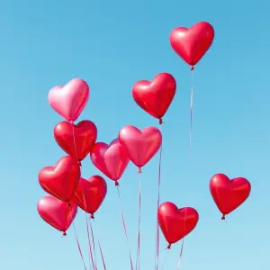 Red and Pink Heart-Shaped Balloons Floating Against Blue Sky