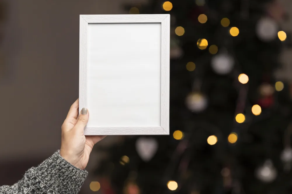 Hand Holding Blank White Photo Frame with Christmas Tree Lights Background