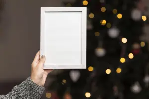 Hand Holding Blank White Photo Frame with Christmas Tree Lights Background